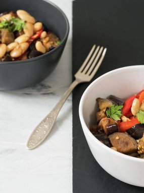 Masada lezzetli haşlanmış patlıcan ve haşlanmış fasulye ve kırmızı biber, kişniş bir prig ile süslenmiş yemekler vardır. Siyah beyaz tabaklar, siyah beyaz arka plan. Close.