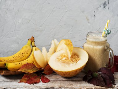 Kavun ve muz ile Smoothie. Muz yanında ahşap bir tabak üzerinde olgun kavun sulu dilimleri. Sonbahar yaprakları ile dekore edilmiştir. Beyaz-sarı renk hamuru ile kavun çeşitli. Ahşap vintage arka plan.