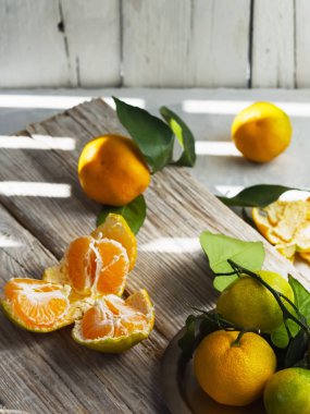Taze, olgun mandalinalar ya da hafif ahşap bir yüzeyde yapraklar ve mandalina dilimleriyle mandalinalar. Yakın plan. Citrus. Güneş ışığı çizgileri.
