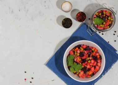 Geleneksel salata - mavi peçetedeki beyaz kasede salata. Yakınlarda bir kavanoz sirke ve baharat var. Gri bir arka planda. Üst Manzara. Boşluğu kopyala.