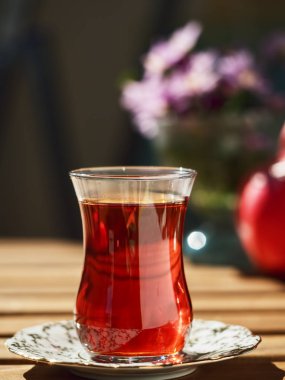 Loggia 'daki ahşap bir masanın üzerinde, çay bardağında çay. Arka planda çiçekler ve olgun nar var. Parlak güneşli bir gün. Yakın plan..