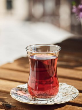 Loggia 'daki ahşap bir masanın üzerinde, çay bardağında çay. Arka planda çiçekler var. Parlak güneşli bir gün. Yakın plan..