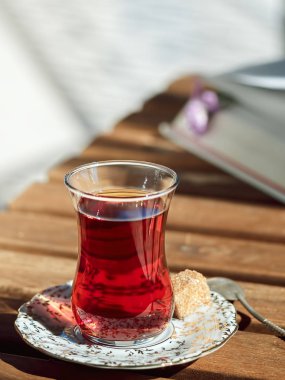 Bir fincan çay, bir fincan çay, bir fincan çay. Yakınlarda bir kaşık şeker ve kaşık. Masanın üzerinde açık bir kitap var, dinlenme zamanı. Parlak güneşli bir gün. Yakın plan..