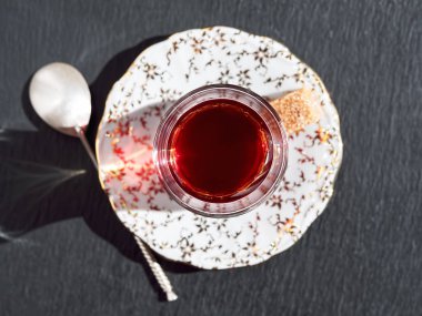 Siyah taştan bir arka planda, çay fincanındaki fincan altlığı. Bir kaşık şeker ve kaşık parçasının yanında. Parlak güneşli bir gün. Üst görünüm.