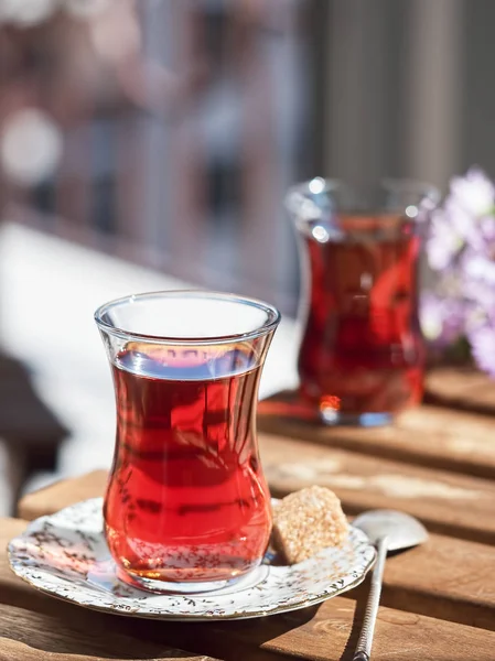 Loggia 'daki ahşap bir masada bulunan bir tabağın üzerinde iki bardak Armudu çayı. Bir parça kamış şekeri ve çay tabağında bir kaşık. Kukgu masasında bir buket kır çiçeği. Parlak güneşli bir gün. Yakın plan..