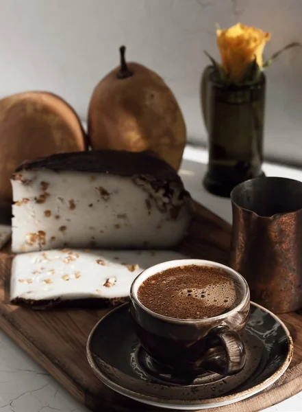 Cup with dark espresso on a gray background. Near cezve, homemade (craft) goat cheese with walnuts and ripe pears. Close up, dessert concept.