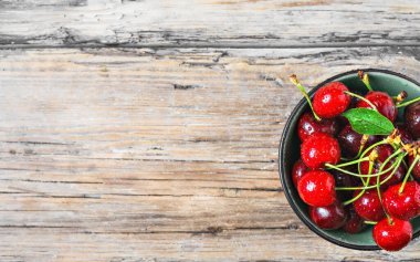 Taze kiraz meyveleri ve siyah bir kâse içinde hafif, ahşap bir masada su damlaları. Kopyalama alanı olan düz düzen.