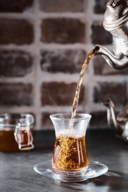 Geleneksel bardakta Türk kırmızı aromatik çayı - koyu tuğlalı armudu. Çaydanlıktan gelen çaydanlık bir bardağa doldurulur. Yakın plan, yüzeysel alan derinliği, kopyalama alanı. Buhar çay bardağının üzerinden yükselir.