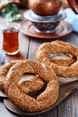 Susam tohumlu taze pişmiş simit ürünleri (Türk simidi - Gevrek veya Kuluri). Kahvaltı için susamlı geleneksel beyaz ekmek, ahşap bir masada kırmızı çay ile bir bardak armudu.