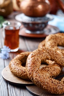 Susam tohumlu taze pişmiş simit ürünleri (Türk simidi - Gevrek veya Kuluri). Kahvaltı için susamlı geleneksel beyaz ekmek, ahşap bir masada kırmızı çay ile bir bardak armudu.