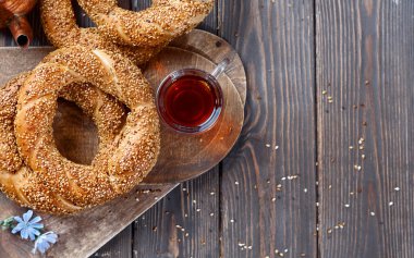 Tahta bir masada taze pişmiş simit - kopya alanı olan susamlı çörek düzlüğü (Türk simidi - Gevrek veya Kuluri). Kahvaltı için susamlı geleneksel beyaz ekmek, bir bardak çayın yanında..
