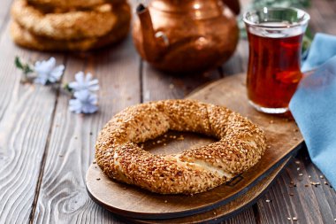 Susam tohumlu taze pişmiş simit ürünleri (Türk simidi - Gevrek veya Kuluri). Kahvaltı için susamlı geleneksel beyaz ekmek, ahşap bir masada kırmızı çay ile bir bardak armudu.