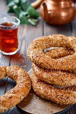 Susam tohumlu taze pişmiş simit ürünleri (Türk simidi - Gevrek veya Kuluri). Kahvaltı için susamlı geleneksel beyaz ekmek, ahşap bir masada kırmızı çay ile bir bardak armudu.