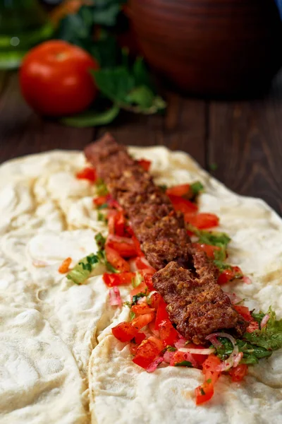Traditional oriental shish - adana kebab, shish kebab with tomatoes on pita bread with vegetables and spices. The process of cooking in the eatery. Turkish cuisine, close-up, shallow depth of field.