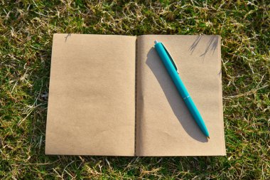 Kalemli boş defter yeşil çimenlerin üzerinde yatıyor