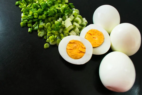 Green onions and boiled eggs for salad on a black background