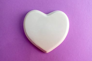 Mor renkte parlak porselen bir kalp, eflatun arkaplan, düğün, düğün kartı, aşk notu. Boşluğu kopyala