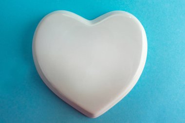 Mavi arka planda beyaz parlak porselen bir kalp, düğün kartı, aşk notu. Boşluğu kopyala