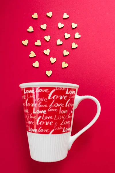 Small wooden hearts fly out of a red cup with an inscription love. Valentine\'s Day, recognition, message.