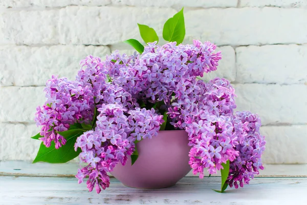 Bouquet of lilac flowers in a lilac vase against the background of a white wall of brick