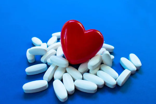 Red heart with pills on a blue background .. Concept of heart disease