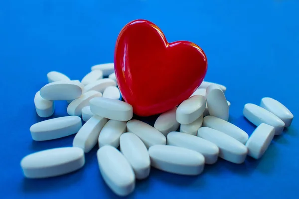Red heart with pills on a blue background .. Concept of heart disease