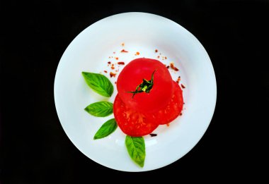 Domates ve fesleğen, siyah bir arka planda beyaz yuvarlak plaka üzerinde spesiyaller ile yaprakları.