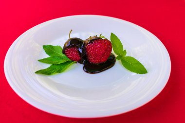 Beyaz bir tabakta çikolata ve nane yaprakları çilek. Kırmızı arka plan, yukarıdan görünüm.