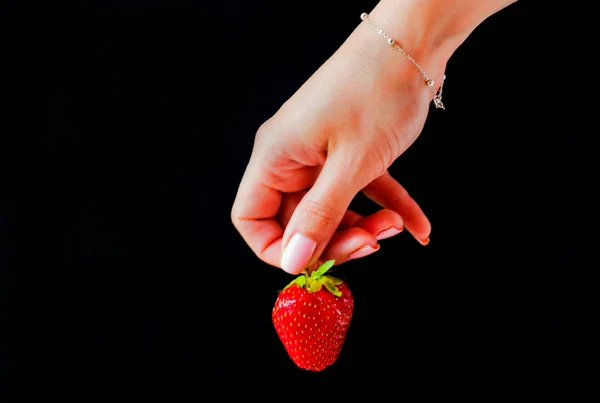 Strawberries on a black background in the hand of a girl.Copy space.