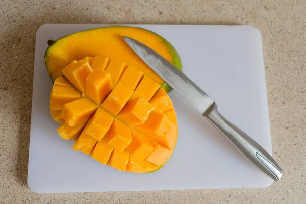 Ripe juicy mango sliced on a white board on a kitchen table.