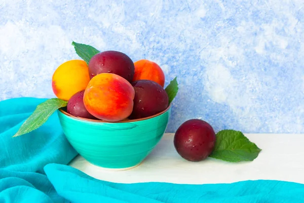 Mavi bir arka planda mavi plakalı olgun erik ve şeftali. Boşluk Kopyala.