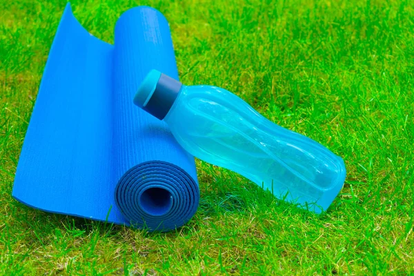 A bottle of water on a yoga mat on fresh green grass. The concept of sports and recreation. Healthy lifestyle. Copy space.