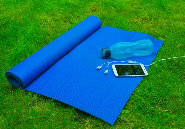 Mat for yoga and sports and a bottle of water on green grass. The concept of training and outdoor recreation A healthy lifestyle. Sport, yoga, fitness, Pilates, fitness equipment.