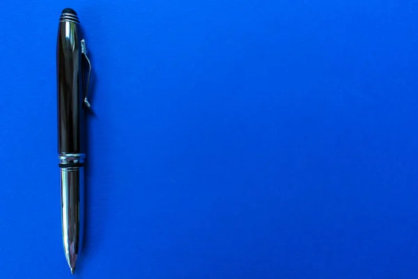 Shiny ballpoint pen on a blue background. Copy space.