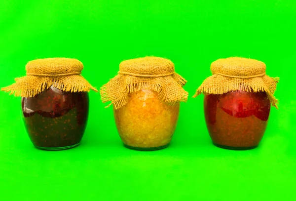 Parlak yeşil bir arka plan üzerinde izole ev yapımı reçel üç kavanoz. Kopyalama alanı.