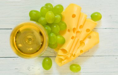 Beyaz ahşap arka plan üzerinde bir tabak üzerinde beyaz şarap, üzüm ve peynir bir bardak. Üstte görüntü