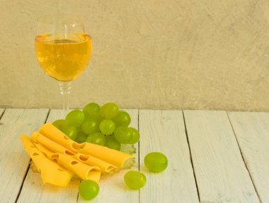 Beyaz ahşap arka plan üzerinde bir tabak üzerinde beyaz şarap ve üzüm ve peynir bir bardak. Kopyalama alanı.