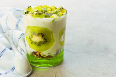 Gri bir arka plan üzerinde kivi yoğurt ve granola ile sağlıklı tatlı.