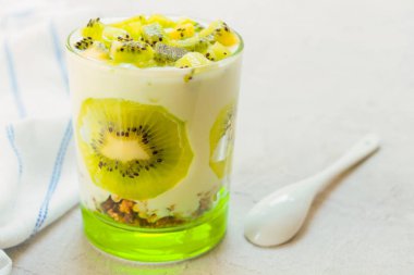 Gri bir arka plan üzerinde kivi yoğurt ve granola ile sağlıklı tatlı.