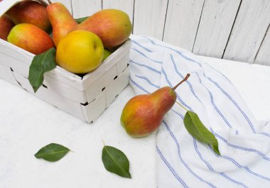 Beyaz ahşap arka plan üzerinde beyaz bir sepet içinde taze organik armut.