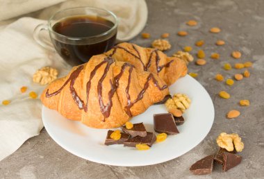 Gri bir arka plan üzerinde kuru üzüm ve fındık ile kahve ve çikolata kruvasan fincan. Kahvaltı konsepti.