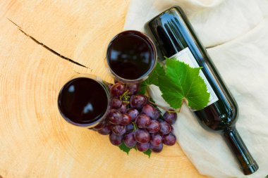 İki kadeh kırmızı şarap ve yeşil çimenlerin arka planı ndaki tahta bir masada bir demet üzüm. Üstte görüntü.