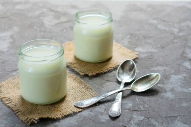 Gri bir arka plan üzerinde bir kavanozda doğal yoğurt. Sağlıklı bir yemek kavramı.