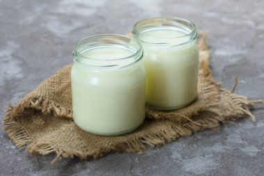 Gri bir arka plan üzerinde doğal yoğurt ve küçük kaşık iki kavanoz. Sağlıklı bir yemek kavramı.