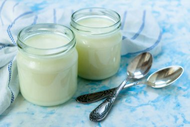 Mavi bir arka plan üzerinde kaşık ile cam kavanozlarda Yunan yoğurt. Sağlıklı gıda kavramı.