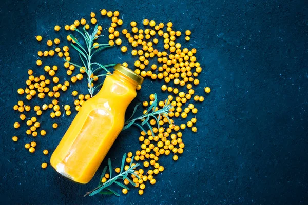  Bir şişe deniz dikenli vitamin suyu ve siyah arka planda taze deniz dikenli meyveler. Yukarıdan görüntüle, boşluğu kopyala.