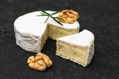 Siyah arka planda biberiye ve ceviz filizi ile süslenmiş şifalı otlu Camembert peyniri..