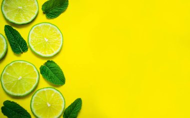 Sarı arka planda limon dilimleri ve nane yaprakları. Boşluğu kopyala.