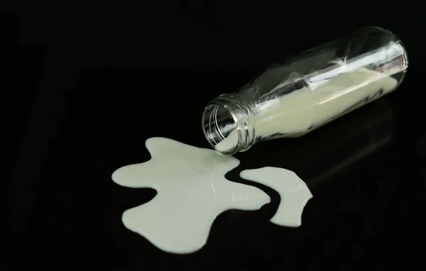 Bottle with spilled milk on a black background. Copy space.