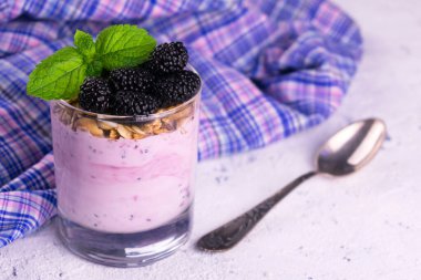Beyaz arkaplanda dut ve tahıl gevreği olan bir bardak yoğurt..